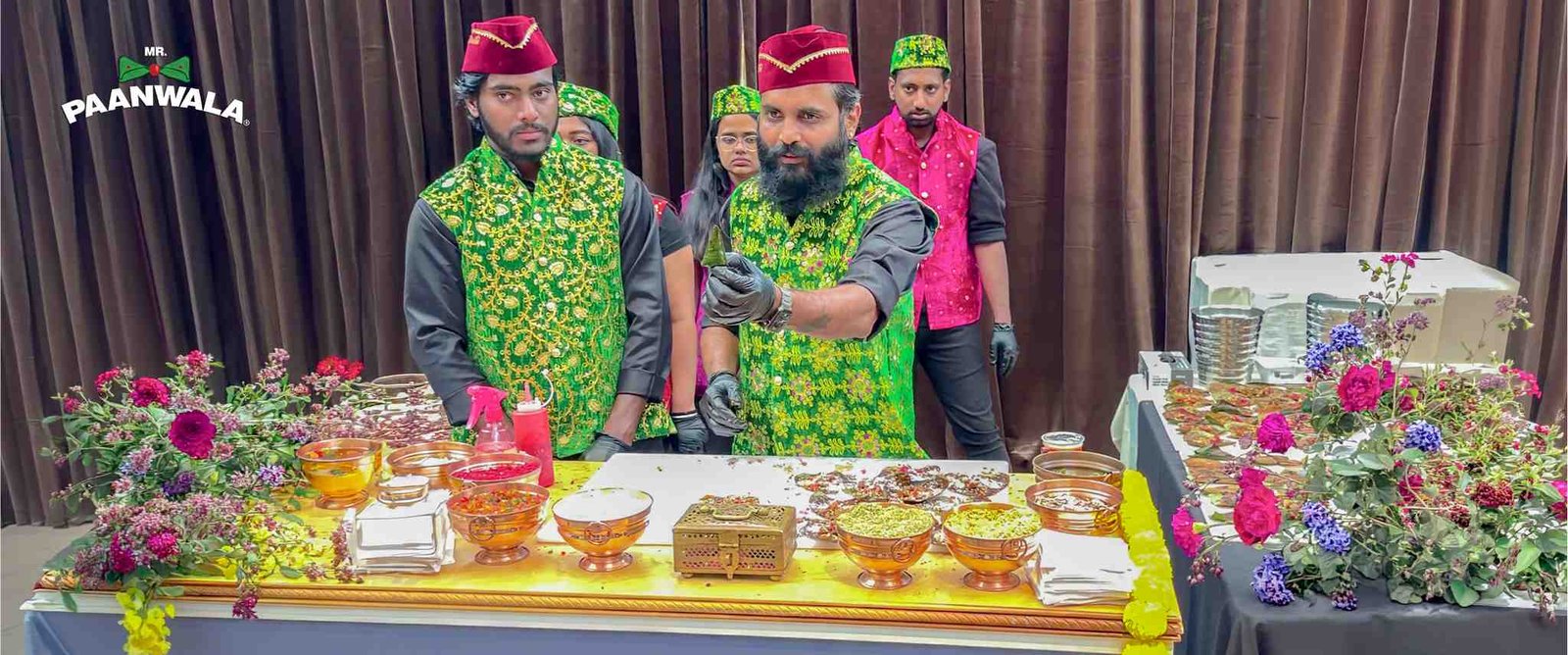 Mr.Paanwala staff preparing paan at a decorated counter while following hygiene practices and wearing gloves.