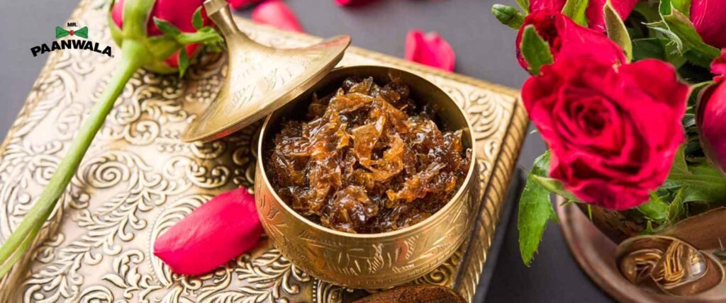 Golden bowl filled with gulkand, a rose petal preserve, surrounded by fresh red roses on an ornate tray.