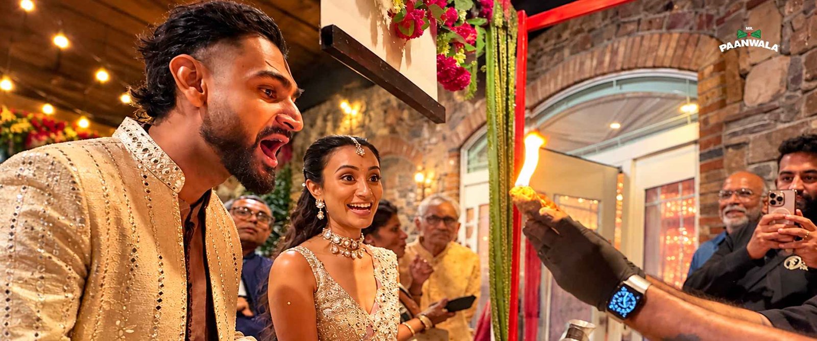 A couple reacts with excitement as a flaming paan is prepared during a festive celebration.