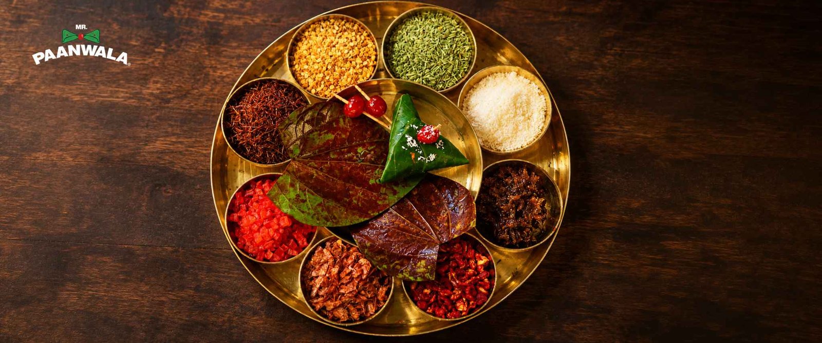 Traditional brass platter displaying betel leaves, gulkand, fennel seeds, coconut, supari, and other paan ingredients.